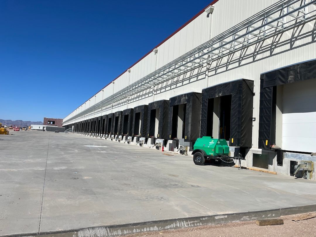 Warehouse loading dock with long white building, empty concrete lot, and a green utility cart under a blue sky