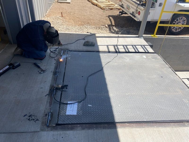 Worker welding a metal ramp at an outdoor construction site, with tools and equipment nearby