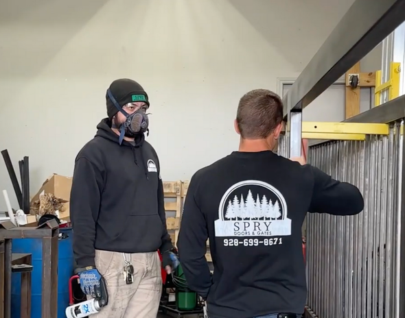 Two people in a workshop inspecting a metal railing beside shelves and tools