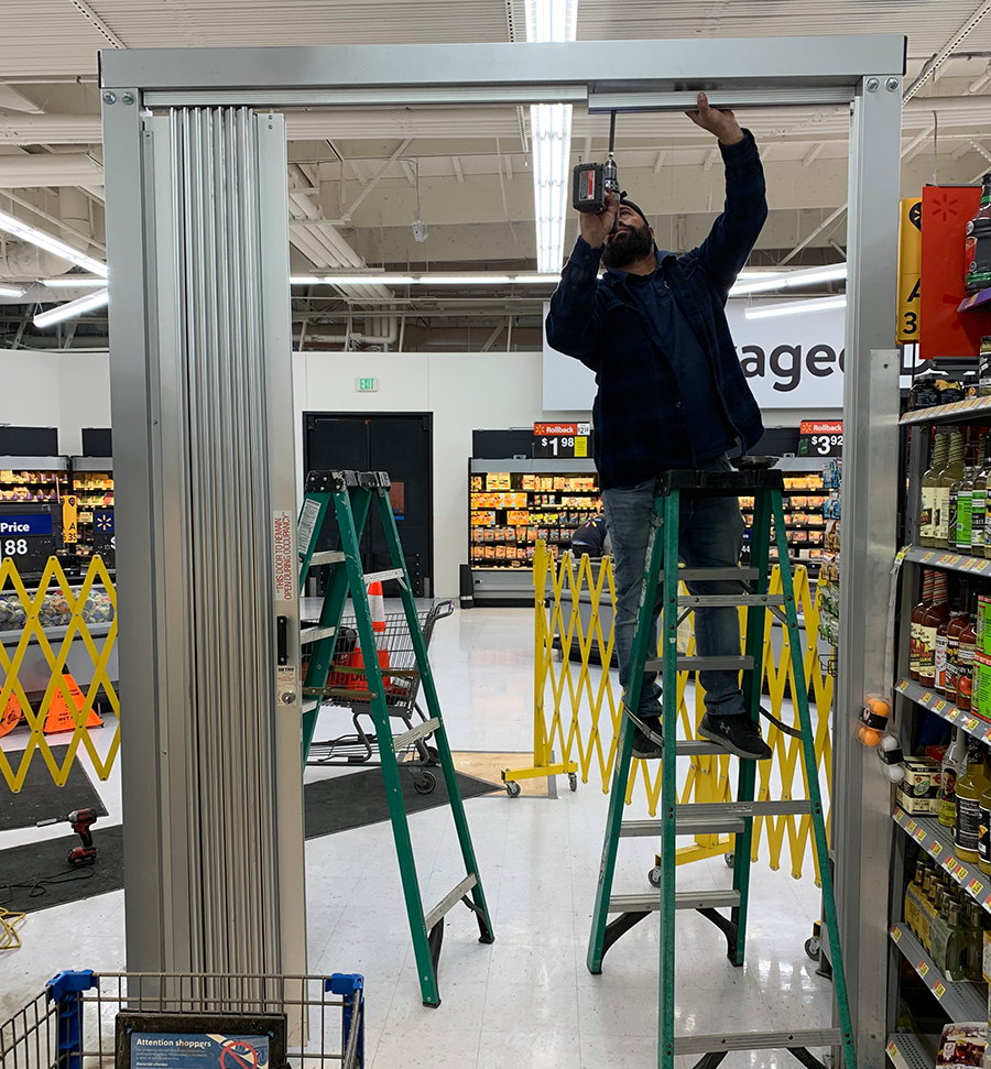 Worker on a green ladder installing a silver frame in a store aisle.