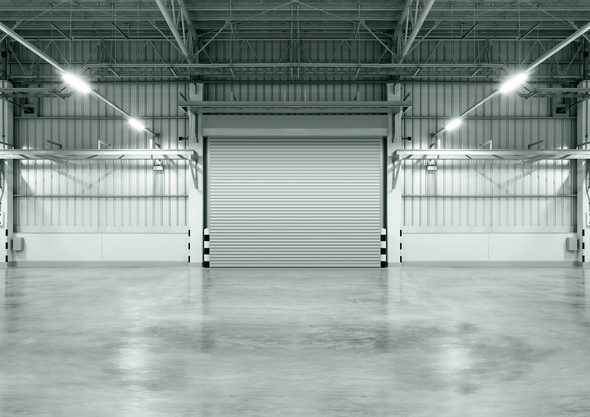 Empty industrial warehouse interior with a closed roll-up door and polished concrete floor