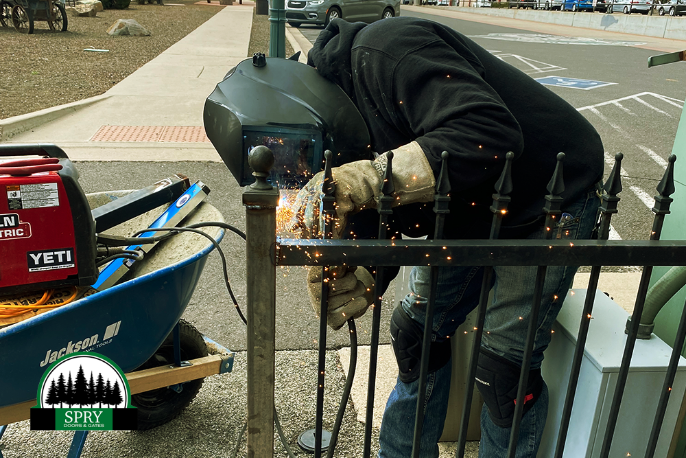 Worker using an angle grinder on a metal railing, sparks flying beside a red welder on a sidewalk.