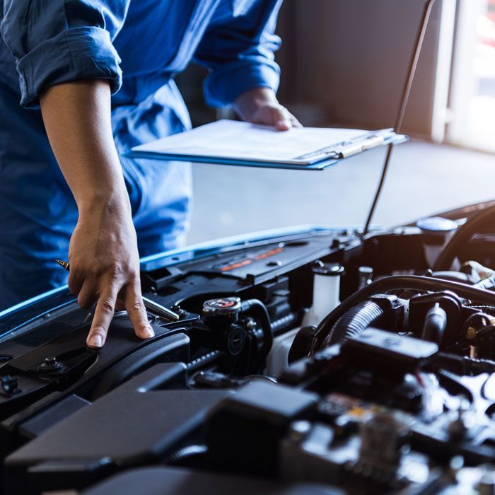 Mechanic in blue shirt inspecting a car engine with a clipboard nearby