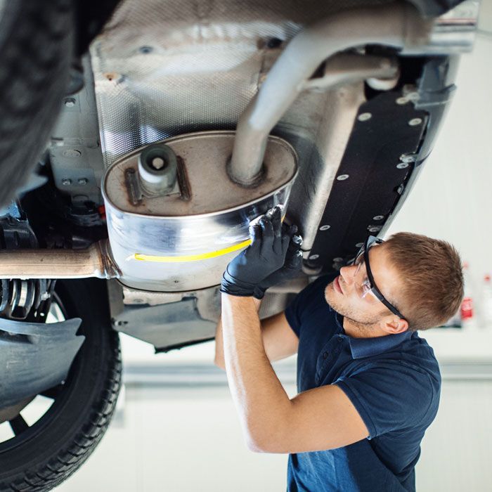 Mechanic inspecting a car’s exhaust and muffler underneath the vehicle