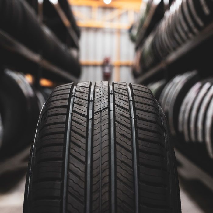 Treaded tire in foreground with rows of tires lined up on shelves in a tire shop