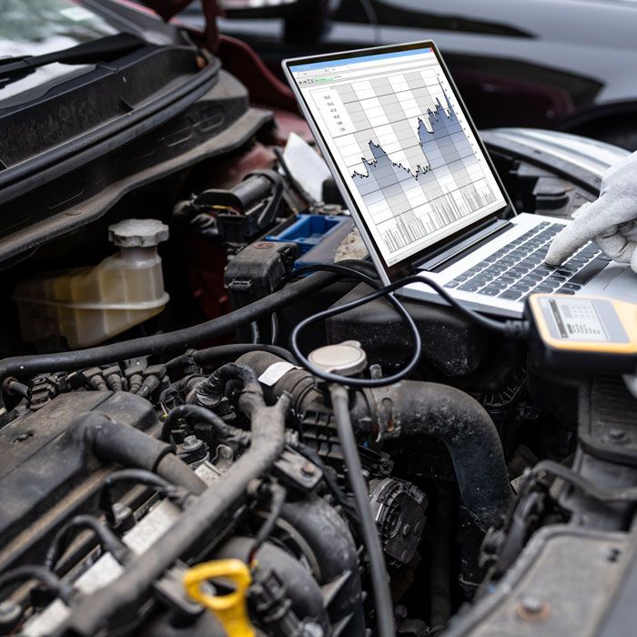 Mechanic diagnosing a car engine with a laptop in the open hood area
