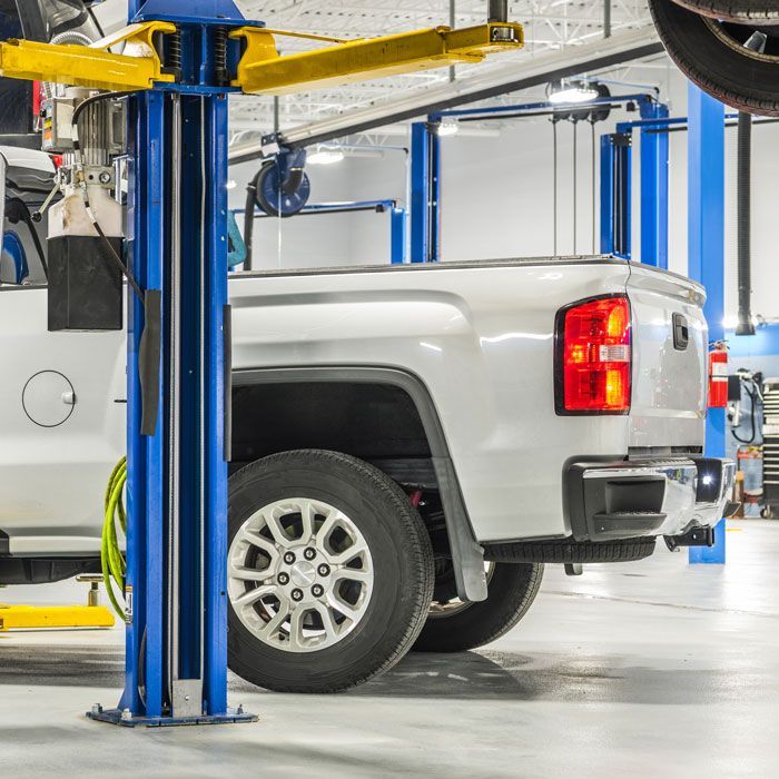 Silver pickup truck on a vehicle lift inside a bright auto repair shop