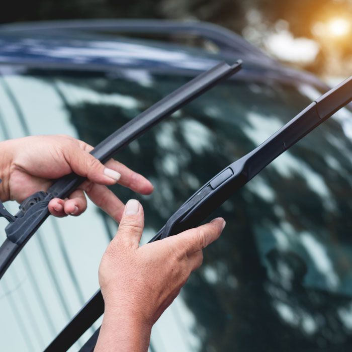 Hands replacing a car windshield wiper on a wet windshield