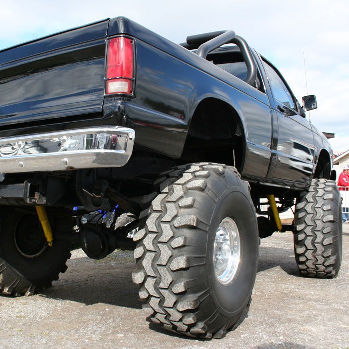 Lifted black pickup truck with oversized off-road tires, viewed from the rear in a parking lot
