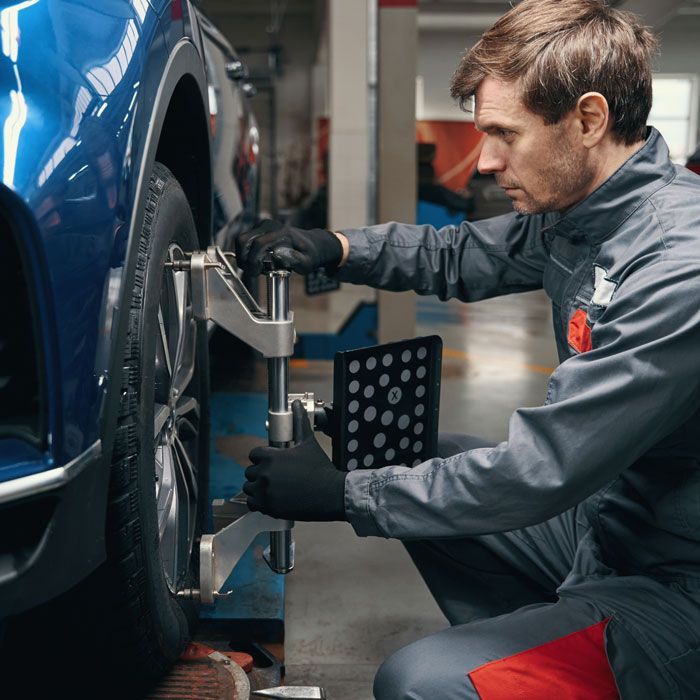 Mechanic aligning a blue car on a wheel alignment machine in a garage