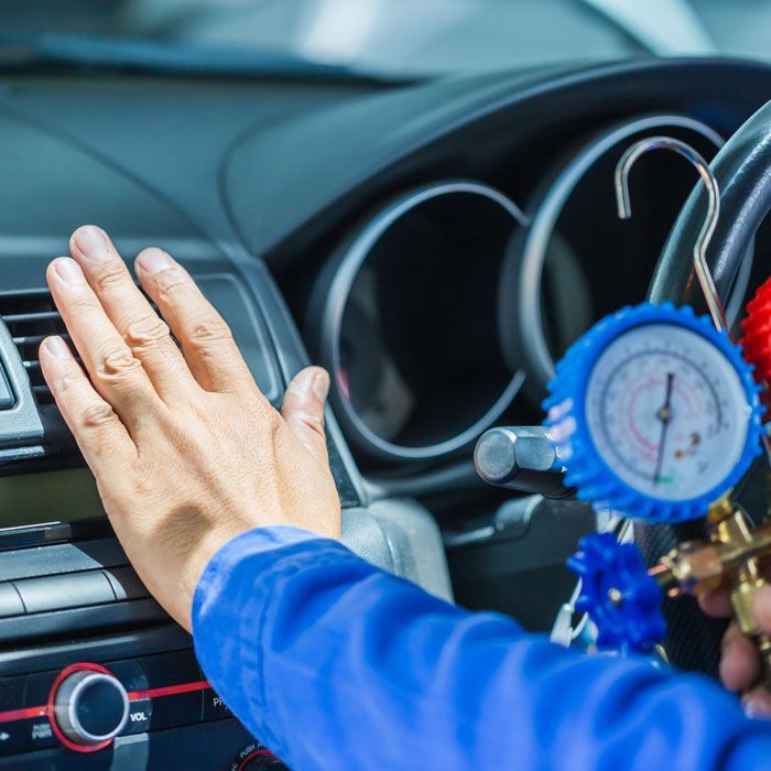 Car mechanic using blue vacuum gauges to inspect a car dashboard and air vents