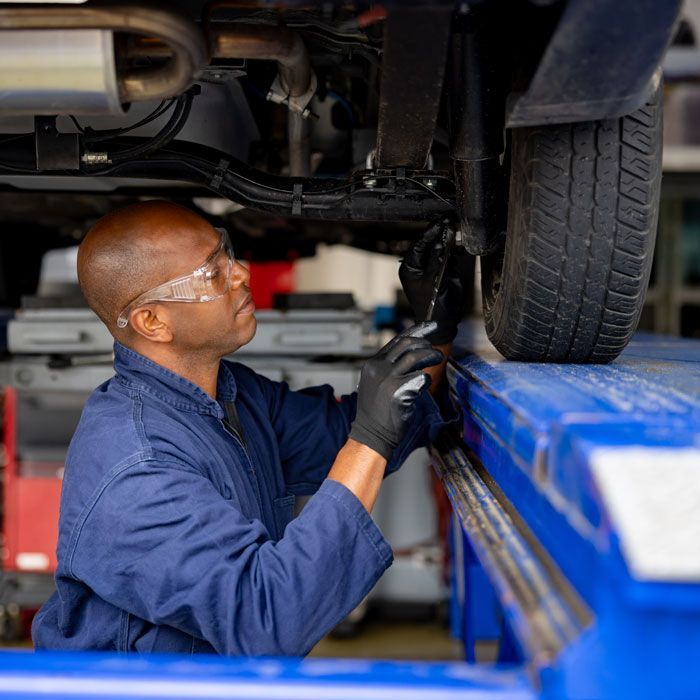 Mechanic in blue coveralls inspects a vehicle’s undercarriage on a lift in a garage