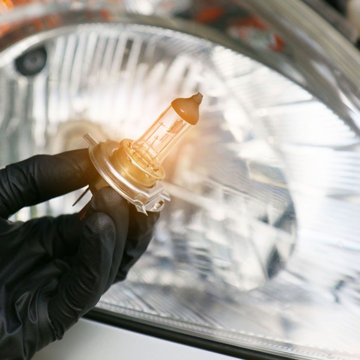 Gloved hand holding a car headlight bulb against a reflective headlamp housing
