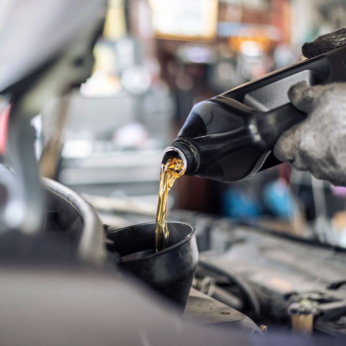 Motor oil pouring from a bottle into a funnel over a car engine