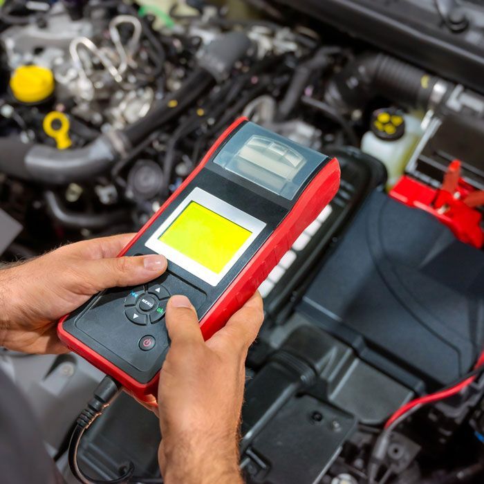 Hands using a red diagnostic scanner to inspect a car engine in a garage