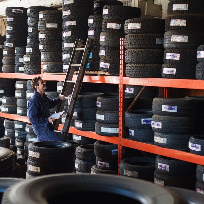 Person stacking tires on warehouse shelves with a ladder and orange racks.