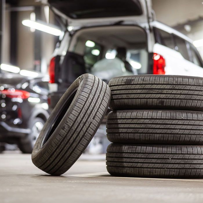 Stacked car tires with one leaning against them in a garage workshop, with vehicles in the background