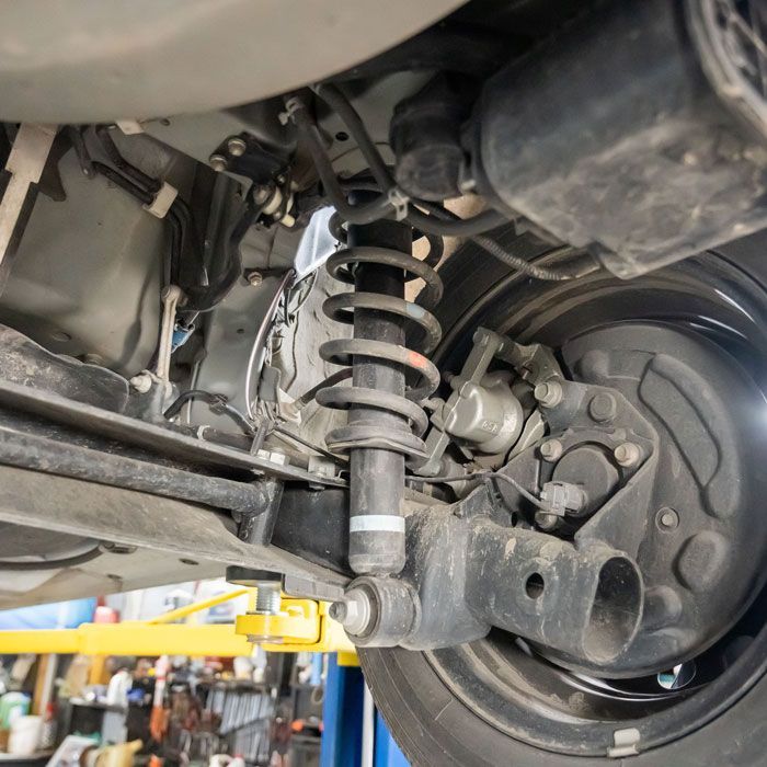 Close-up of a car’s rear suspension, wheel hub, and coil spring on a lift in a garage.