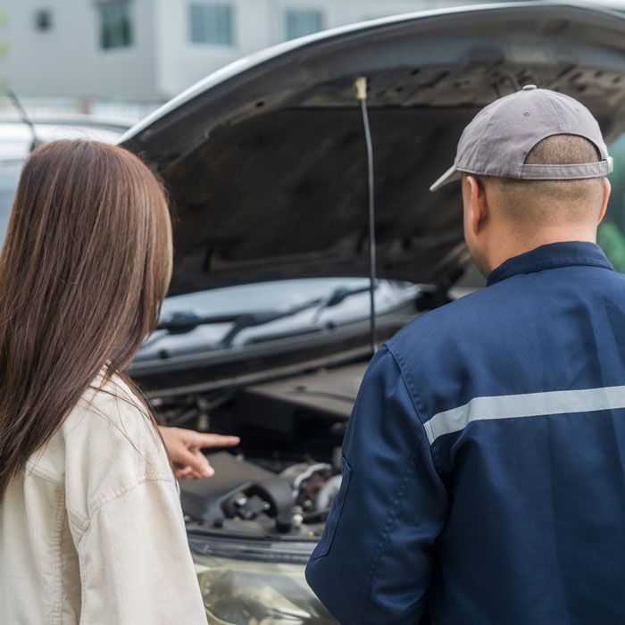 Two people inspecting a car with its hood open on a street