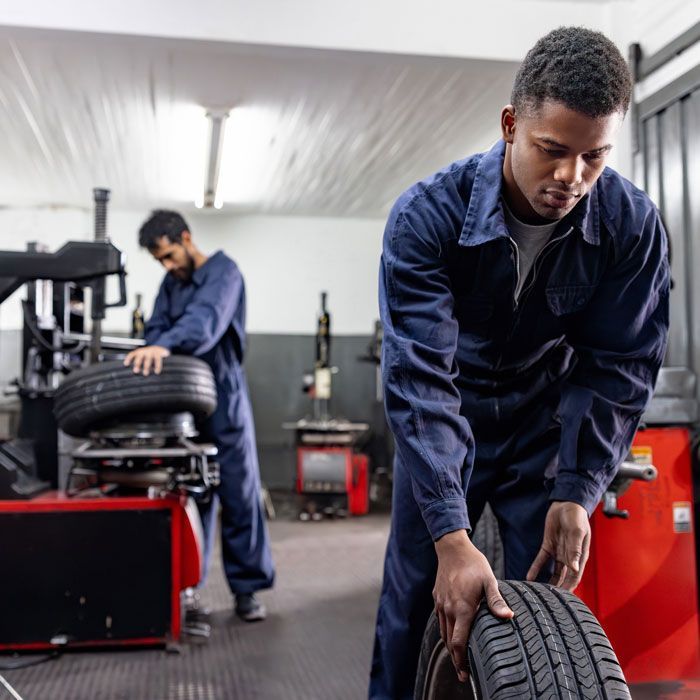 Mechanics aligning tires in a garage, with a red tool cabinet and car lift in the background