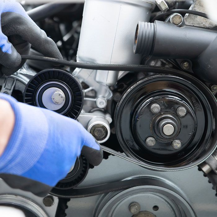 Close-up of a car engine belt and pulleys, with a gloved hand adjusting a component.