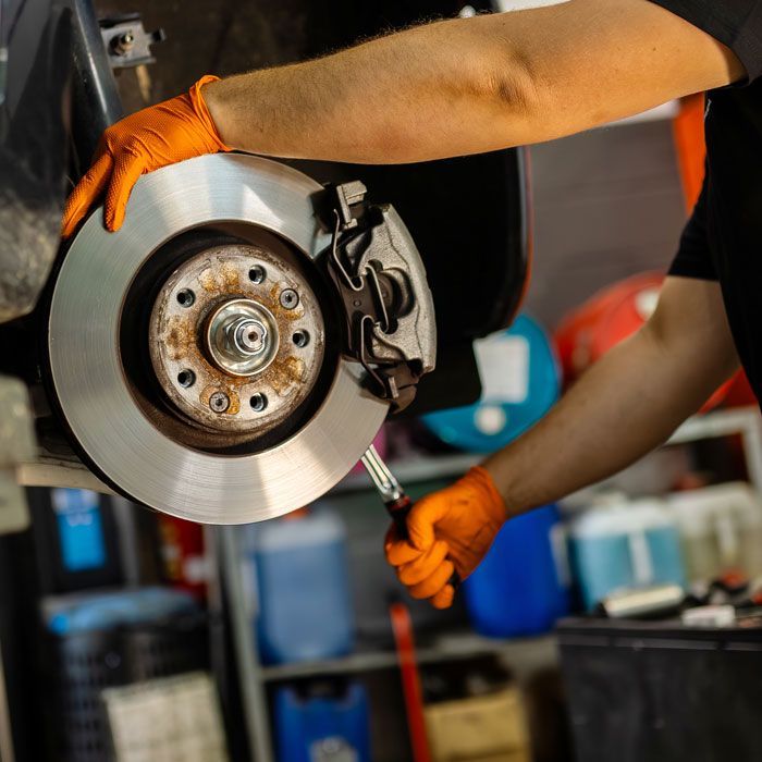 Mechanic in orange gloves replacing a car brake rotor with a wrench