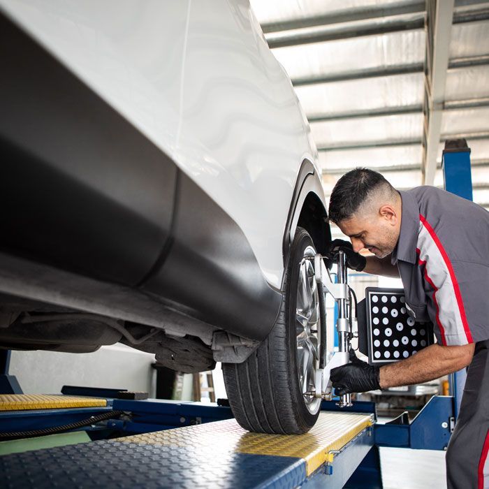 Mechanic inspecting a white car’s wheel in a garage with alignment equipment