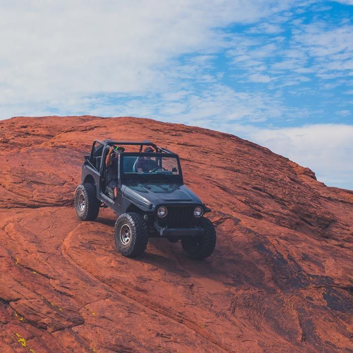 Black Jeep Wrangler driving on a red rock slope under a blue sky