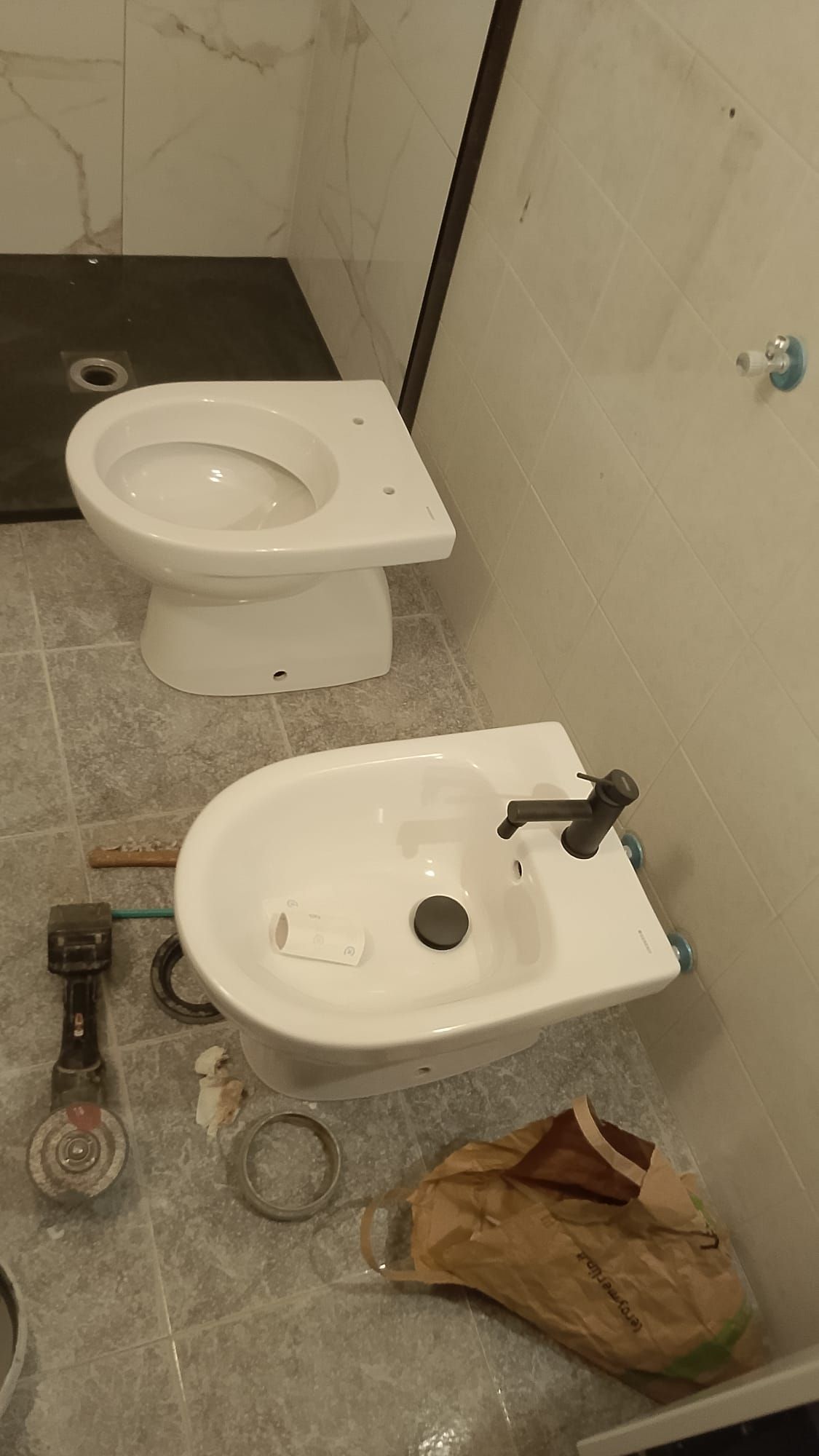 Bagno con due WC in fase di installazione, tubi e attrezzi sparsi sul pavimento.