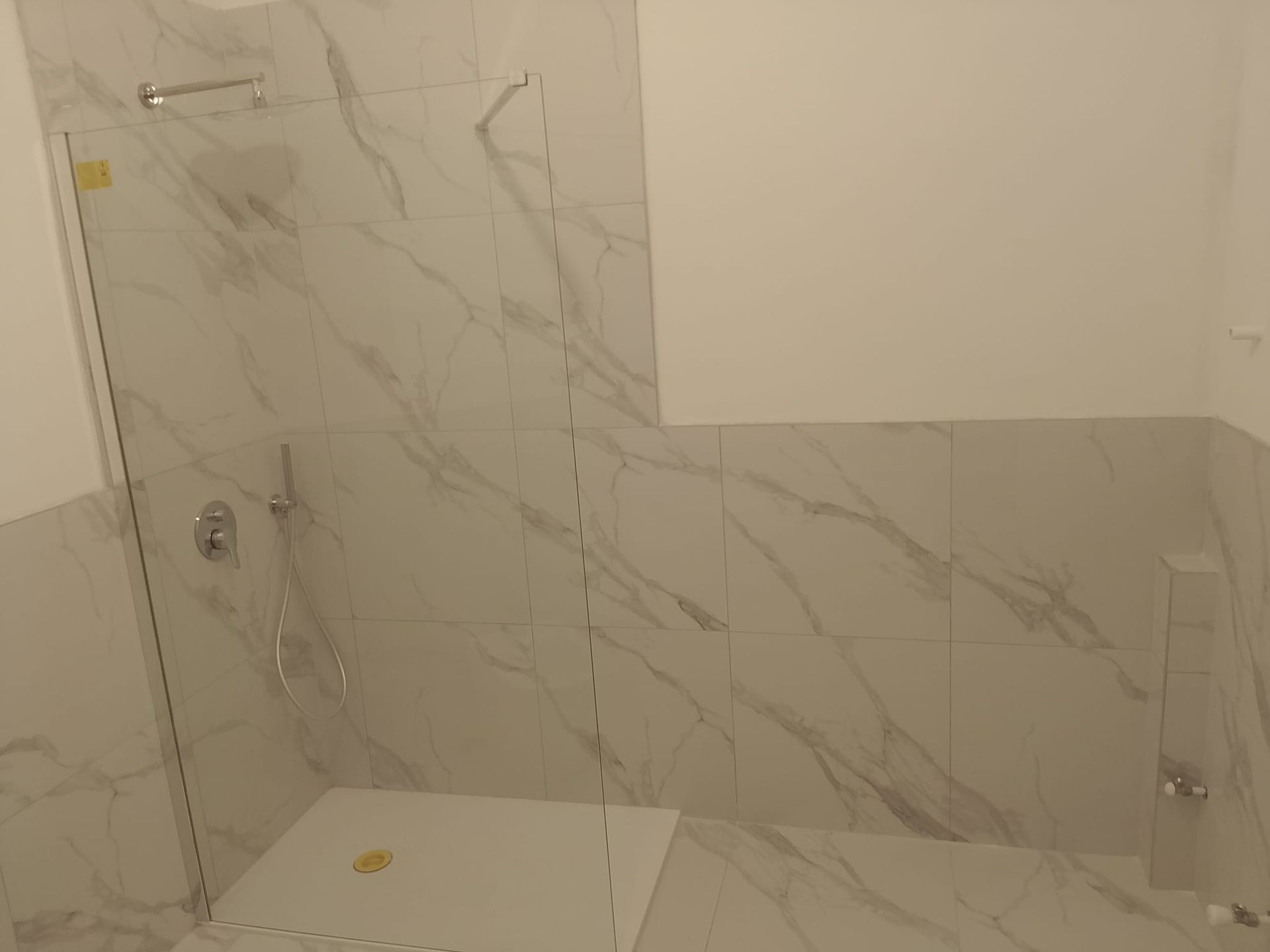 Box doccia vuoto piastrellato con rivestimento a parete effetto marmo e nicchia integrata.