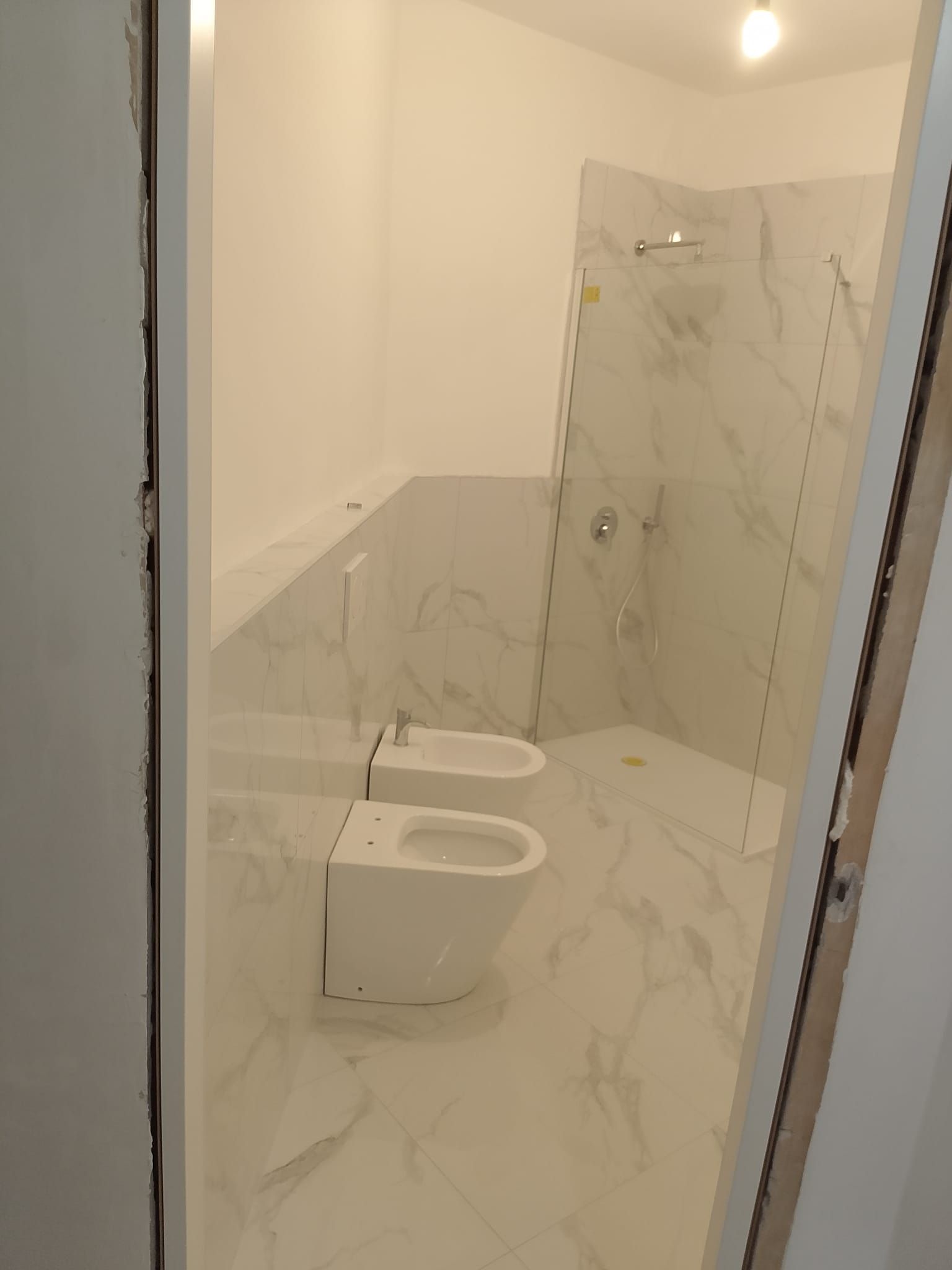 Piccolo bagno piastrellato con bidet a parete, WC e box doccia in vetro.