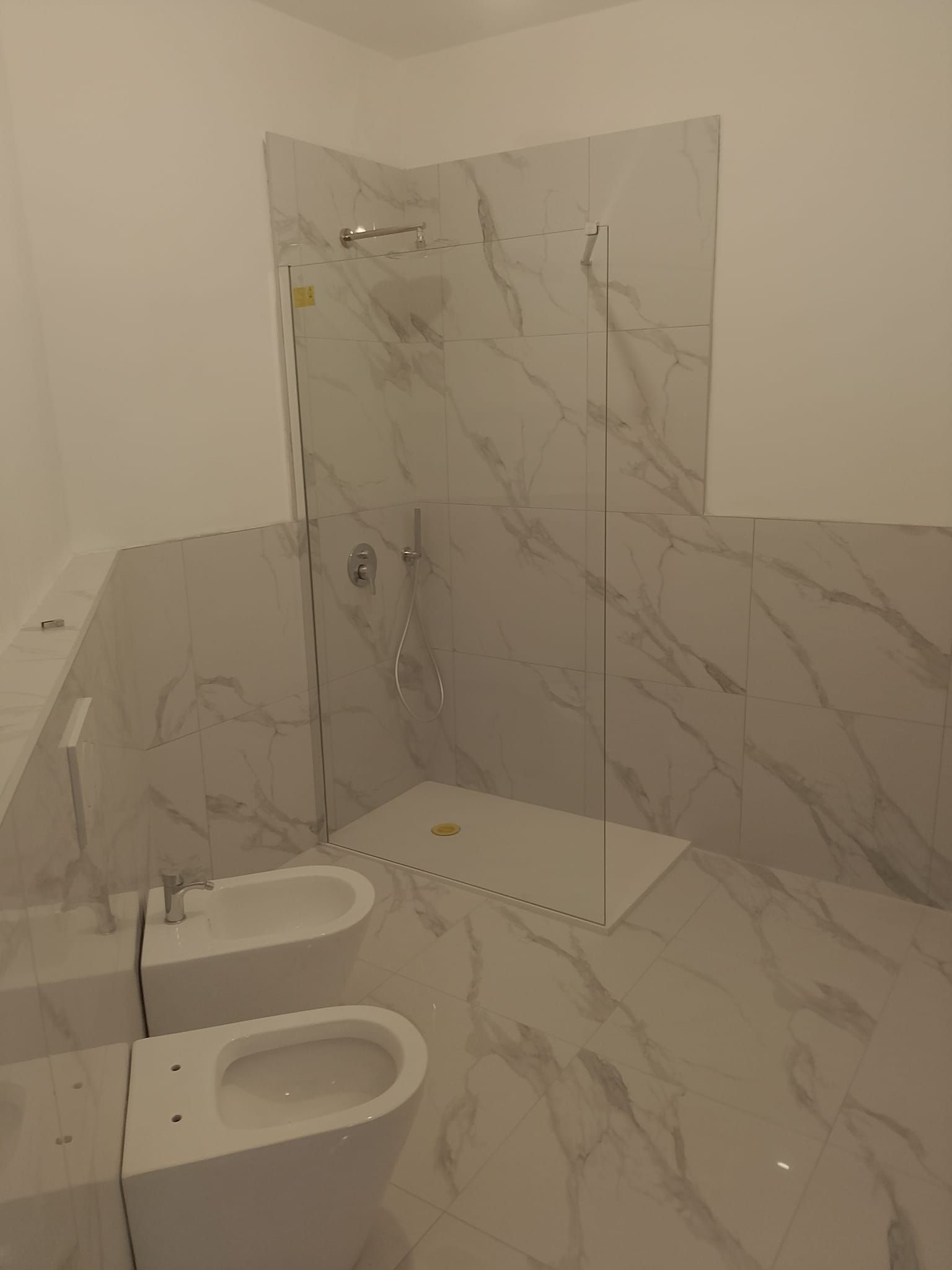 Bagno moderno piastrellato di bianco con bidet, WC e box doccia in vetro.