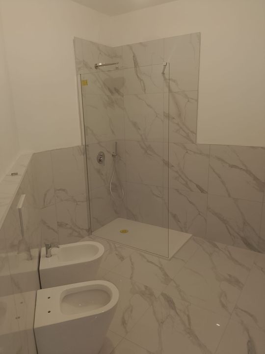 Bagno moderno piastrellato di bianco con bidet, WC e box doccia in vetro.