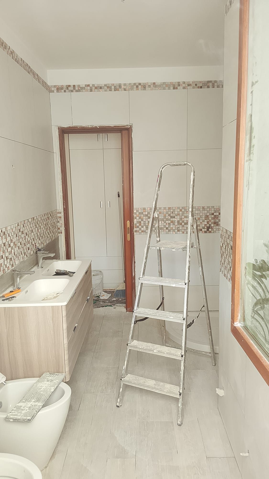 Bagno stretto in fase di ristrutturazione con scaletta, pareti piastrellate e lavandino sulla sinistra.