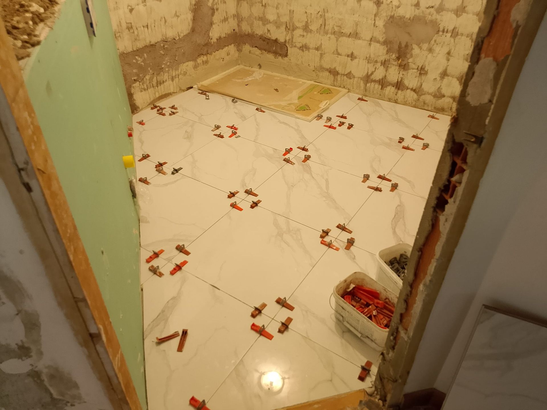 Piccolo bagno piastrellato in fase di ristrutturazione, con pareti non rifinite e materiali edili sul pavimento.