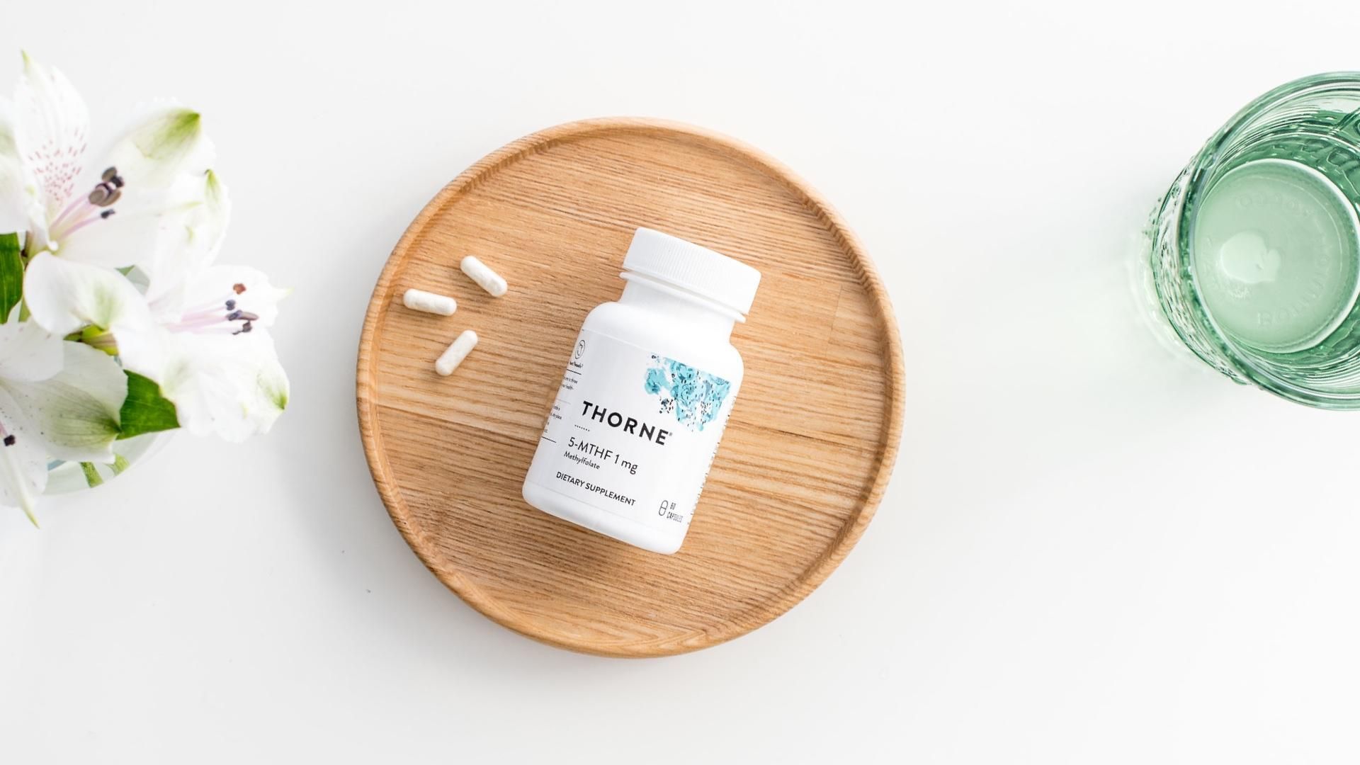 White bottle of supplements on a wooden plate with pills, flowers, and a glass of water.