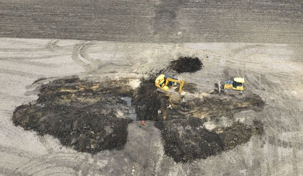 A yellow excavator is digging in the dirt in a field.
