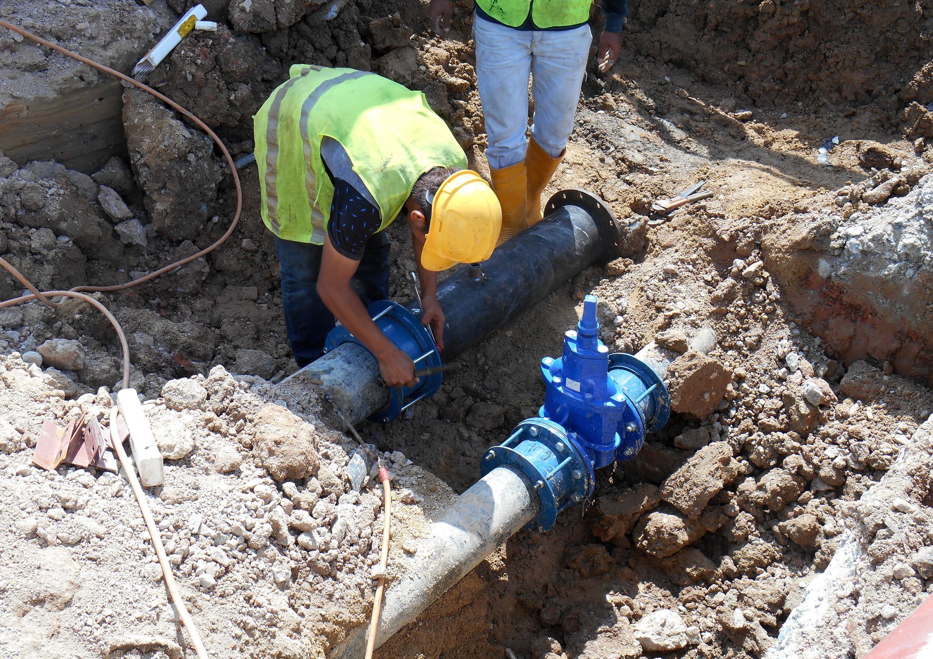 A man in a yellow hard hat is working on a pipe in the dirt.