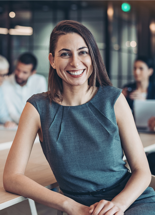 a woman is smiling while sitting at a table in front of a group of people.