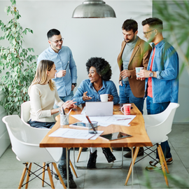 a group of people are sitting around a table with a laptop on it.
