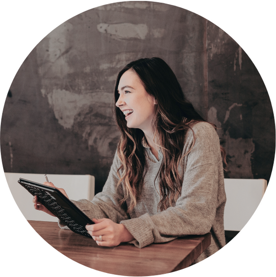 a woman is sitting at a table holding a tablet and smiling.