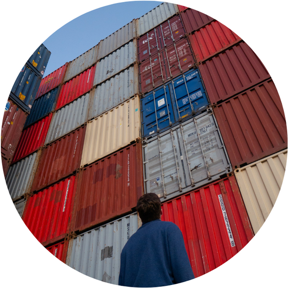 a man in a blue shirt stands in front of a wall of shipping containers.