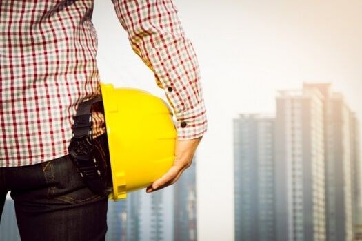 Un trabajador de la construcción sostiene un casco amarillo frente a una ciudad.