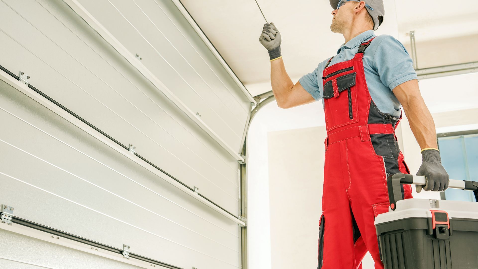 A man in red overalls is working on a garage door.