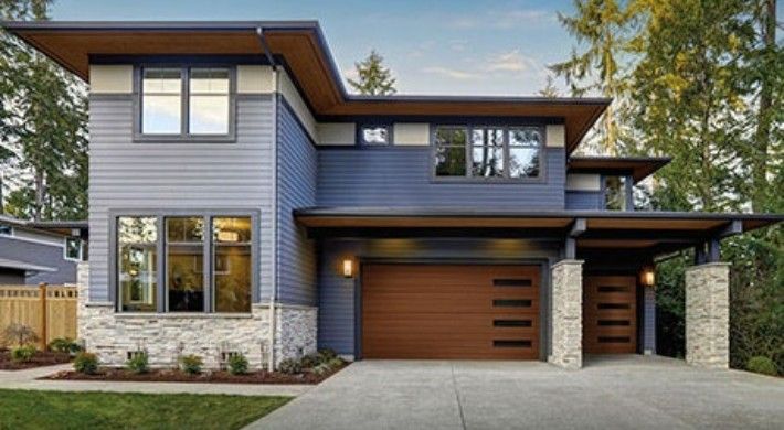 A blue house with a wooden garage door is surrounded by trees.