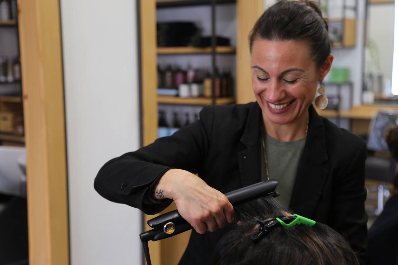 Parrucchiere che liscia i capelli di una cliente con una piastra in un salone