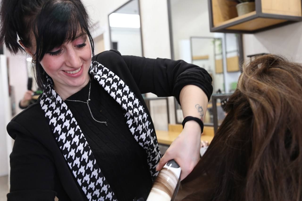 Una parrucchiera arriccia i capelli di una donna in un salone, sorridendo mentre lavora.