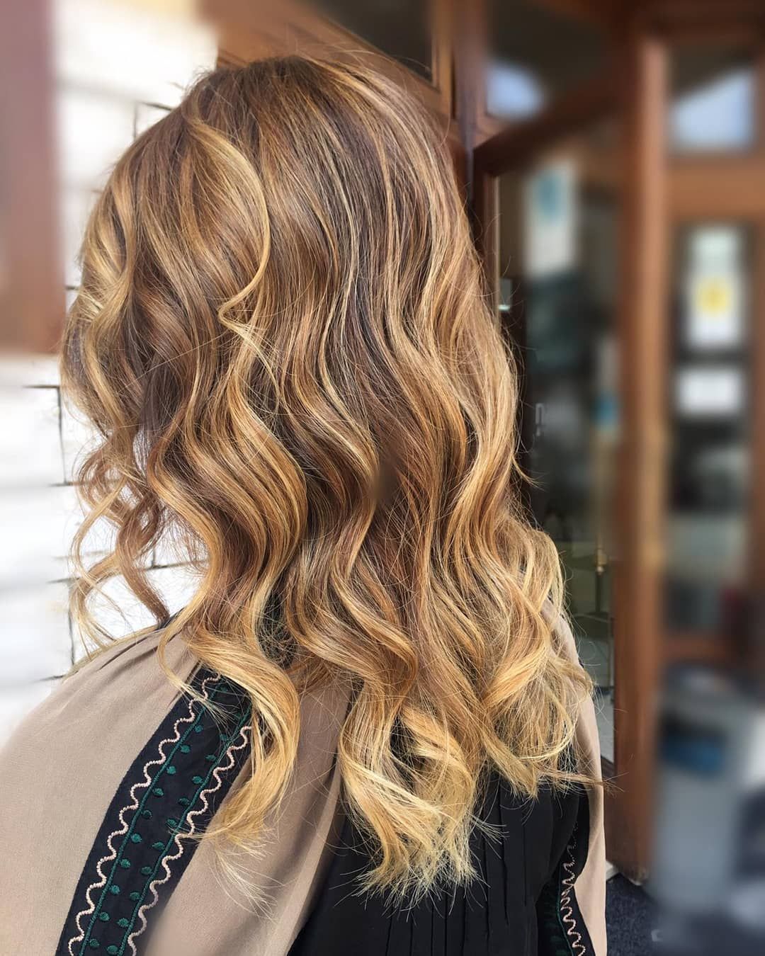 Capelli mossi biondo-castani visti da dietro, con un top nero bordato di pizzo sullo sfondo sfocato di una porta.