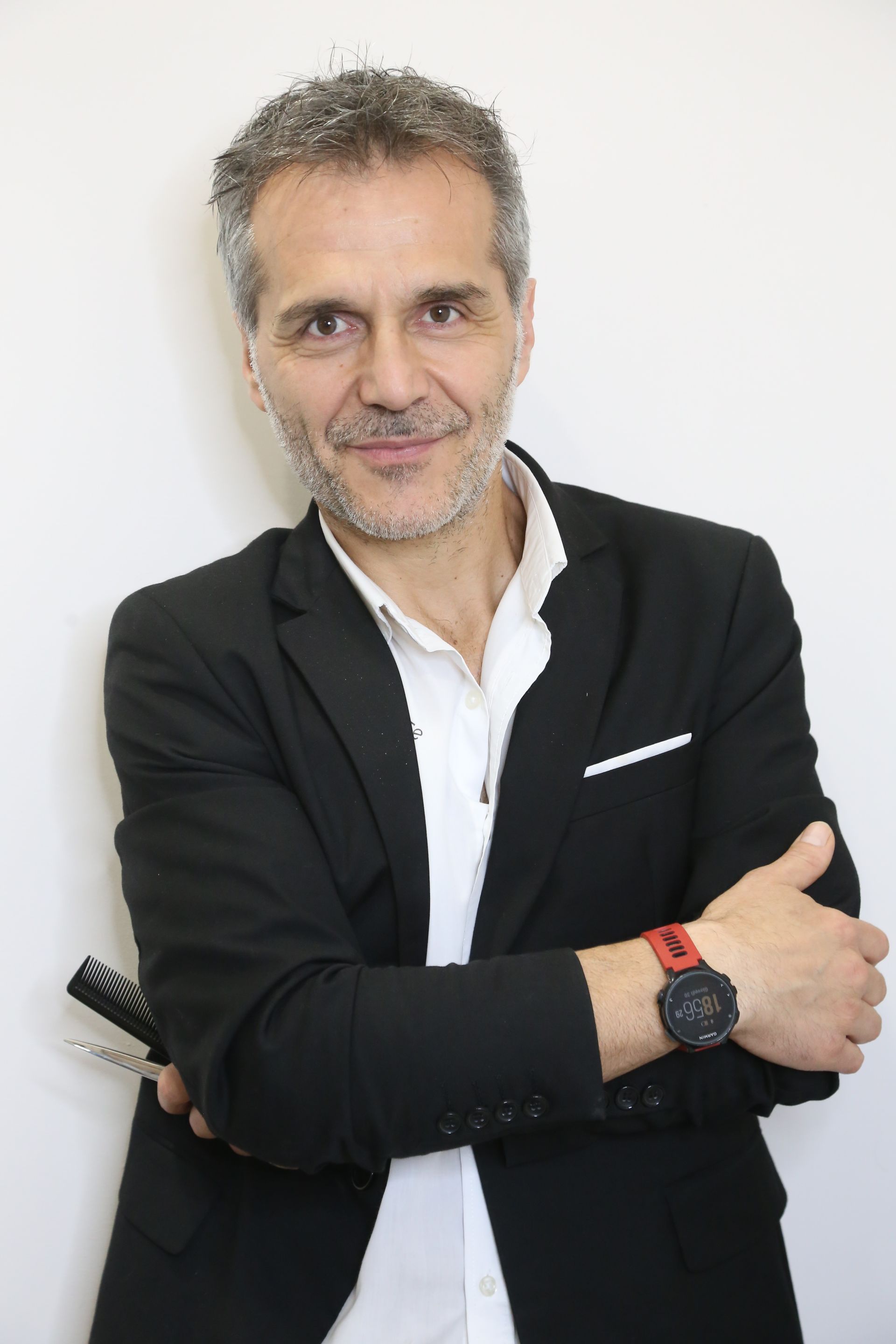 Uomo in blazer nero in piedi con le braccia incrociate, sorridente su sfondo chiaro