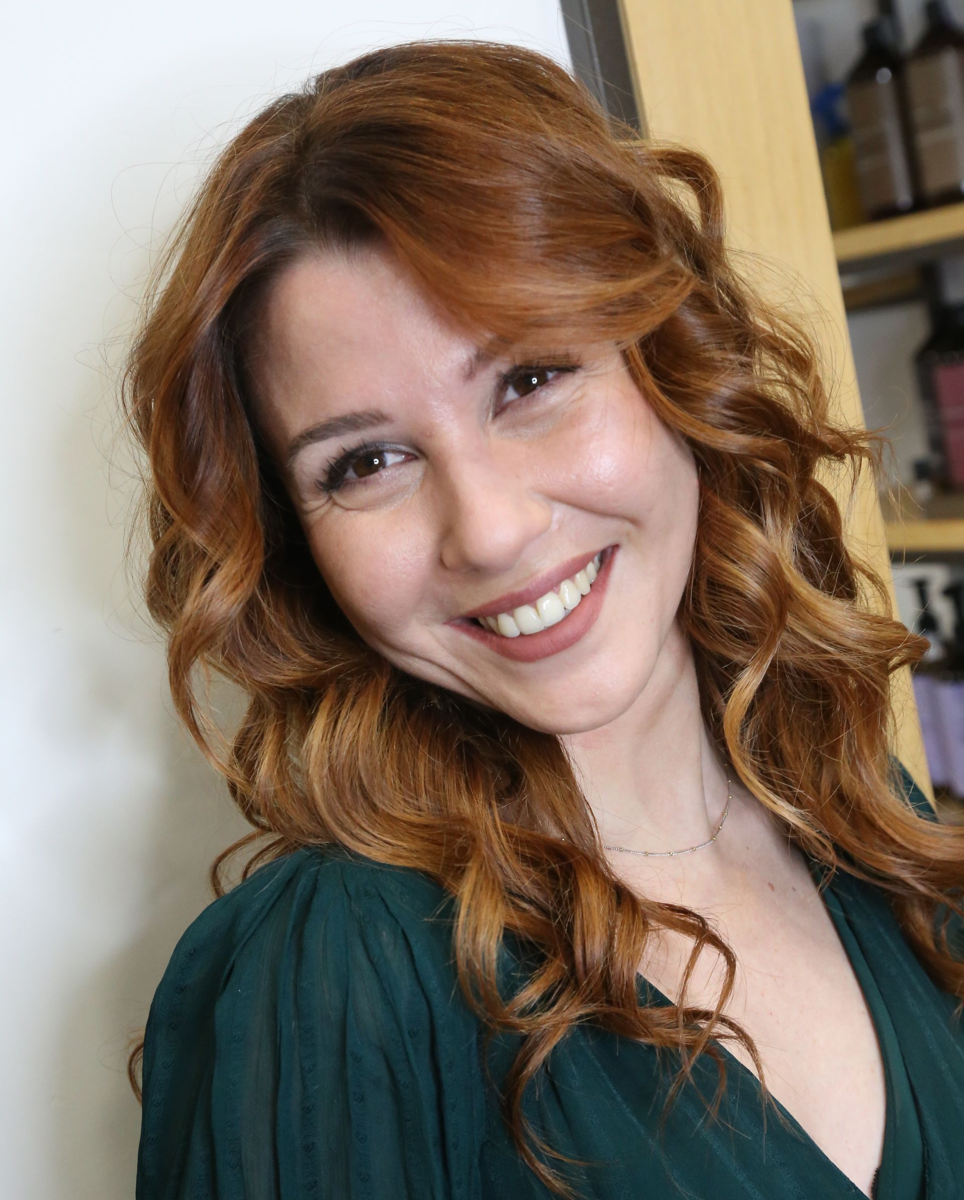 Donna sorridente con capelli mossi color castano ramato, che indossa una maglietta verde scuro